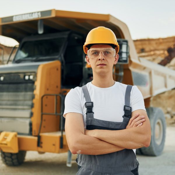 Standing in the front of vehicle. Worker in professional uniform is on the borrow pit at daytime